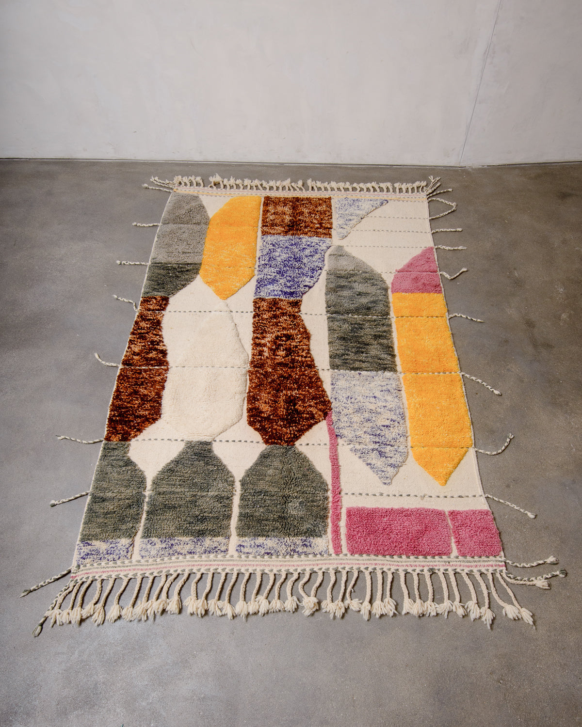 Unique Berberlin Beniourain rug with woven and knotted areas and tassels on all four sides, laying flat on concrete floor.